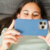 Vesela najstnica leži na kavču in gleda v telefon - odvisnost od socialnih omrežij in umetne inteligence