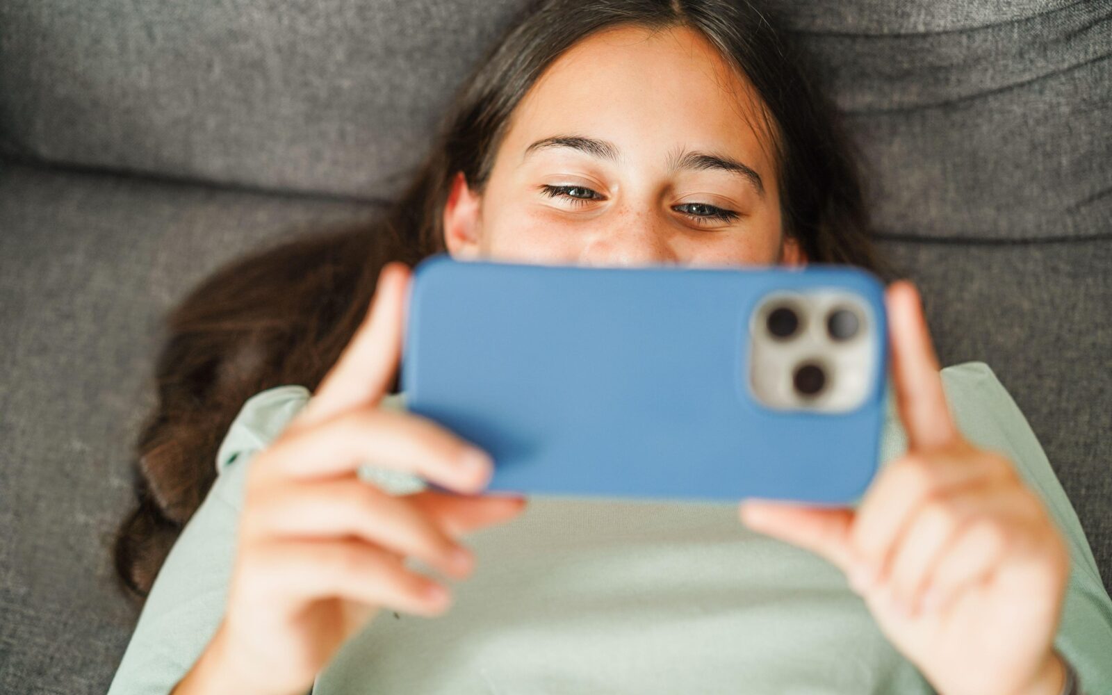 Vesela najstnica leži na kavču in gleda v telefon - odvisnost od socialnih omrežij in umetne inteligence