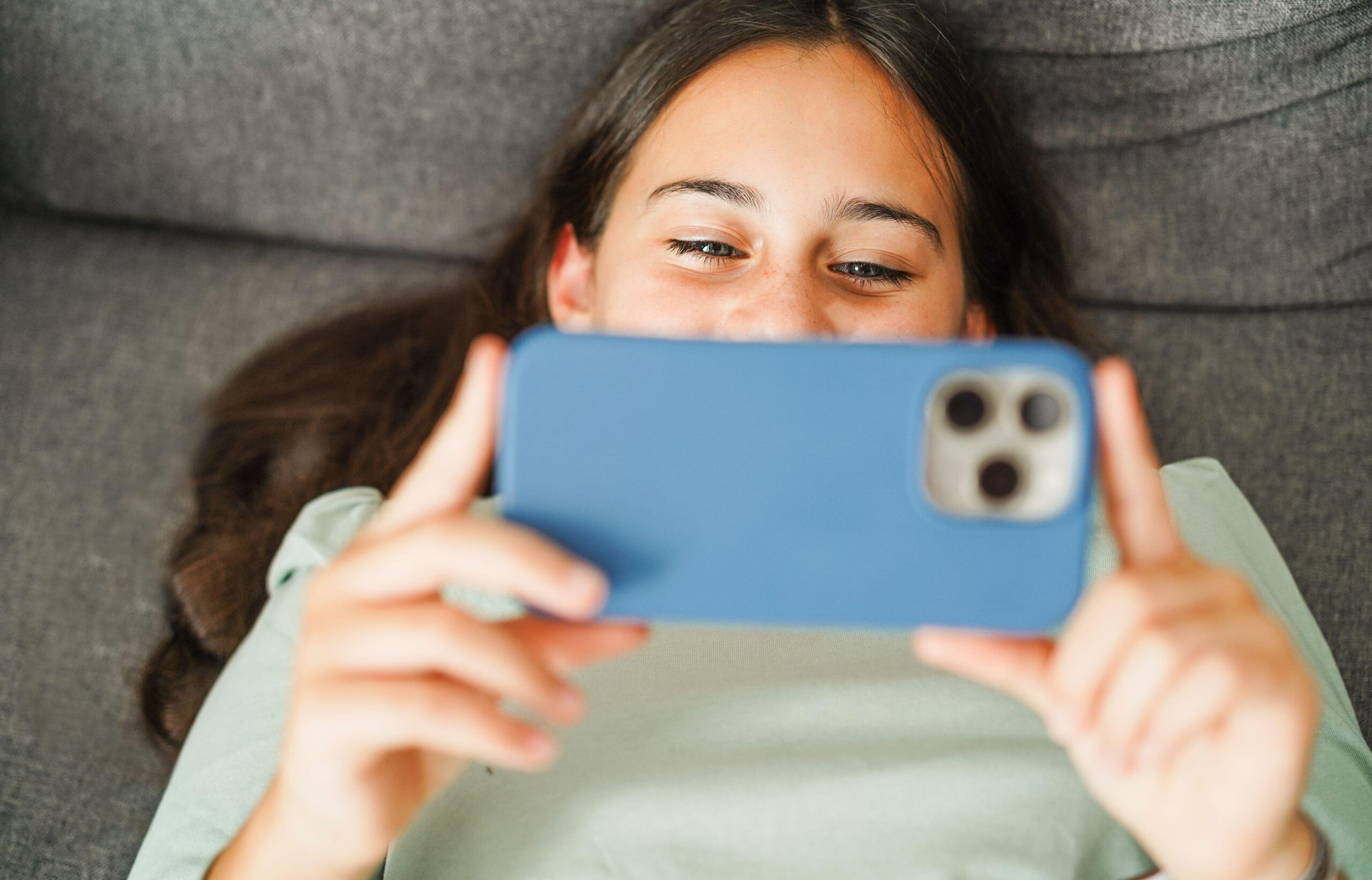 Vesela najstnica leži na kavču in gleda v telefon - odvisnost od socialnih omrežij in umetne inteligence