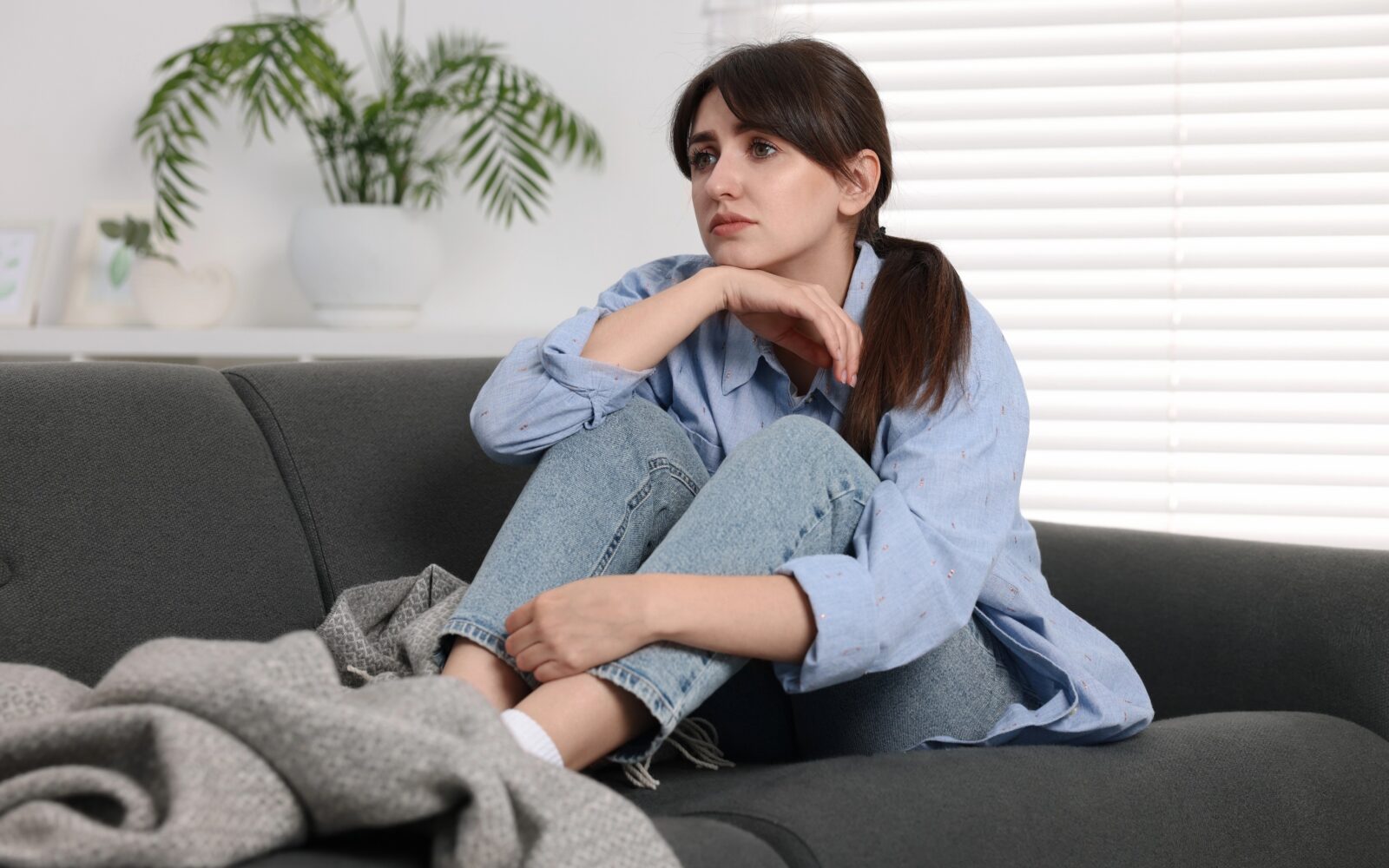 Osamljena, žalostna mlada ženska sedi na kavču
