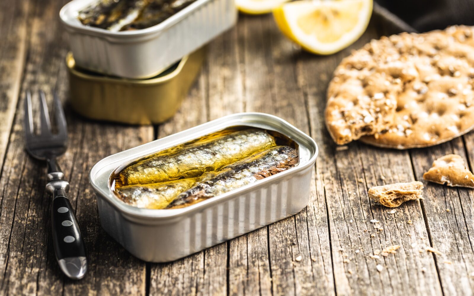 Na mizi so sardine v olju v konzervi, vilica, limone in krekerji