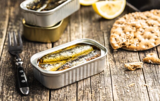 Na mizi so sardine v olju v konzervi, vilica, limone in krekerji