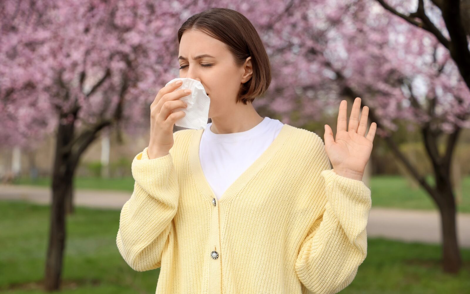 Mlada ženska s senenim nahodom kiha v cvetočem parku