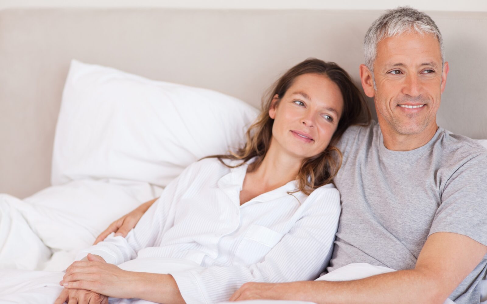 Srečen in nasmejan par v postelji leži objet