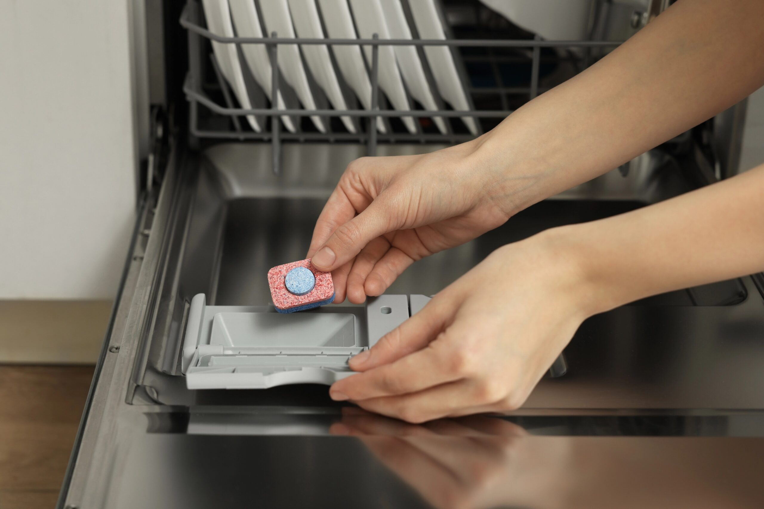 Ženska vstavlja tableto za pomivanje posode v stroj - marsikatere tablete za pomivalni stroj že vsebujejo sredstvo za izpiranje, ki pomaga pri sušenju posode.