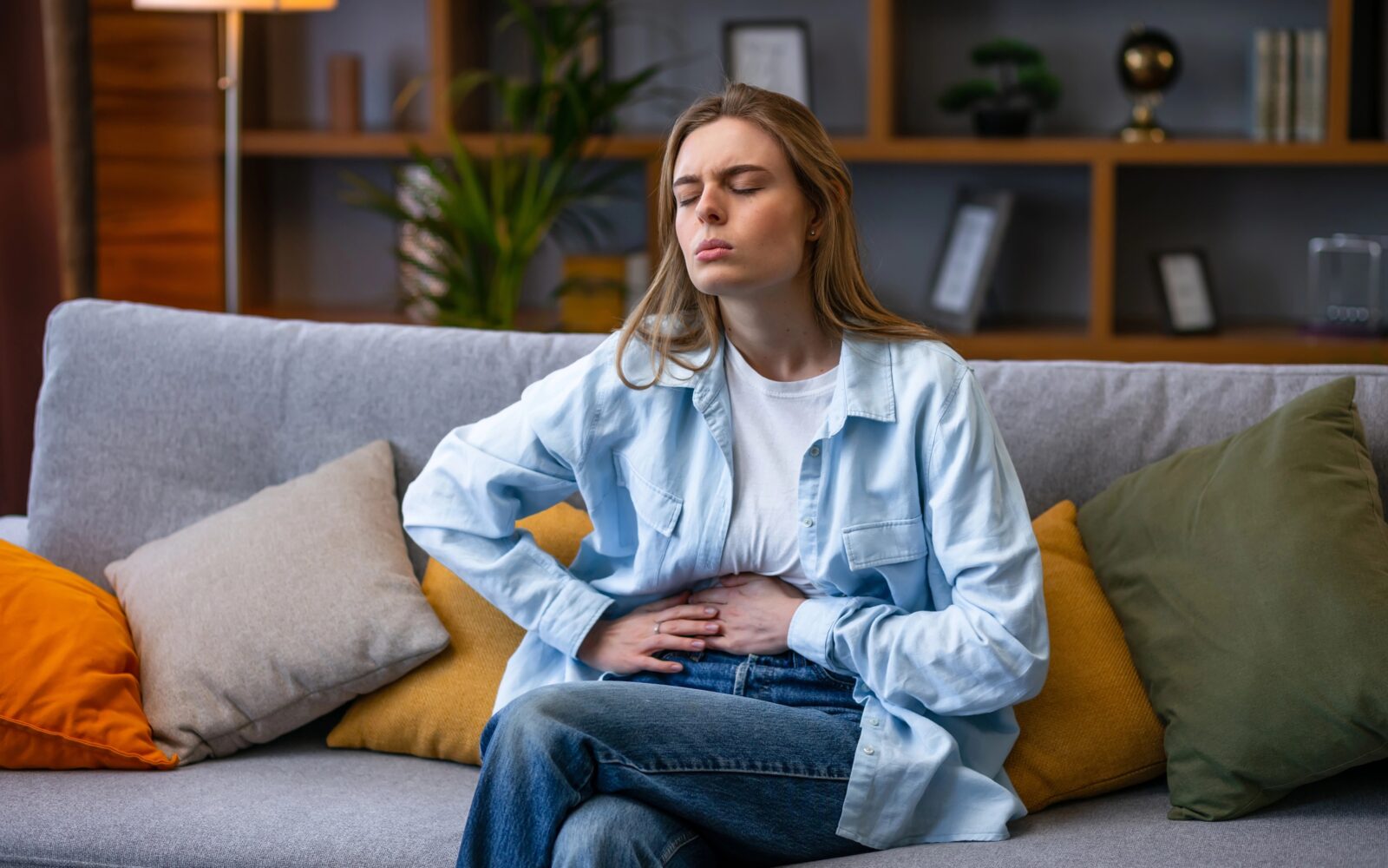 Ženska se na kavču drži za trebuh zaradi bolečin, ki so posledica trebušne viroze.