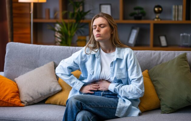 Ženska se na kavču drži za trebuh zaradi bolečin, ki so posledica trebušne viroze.