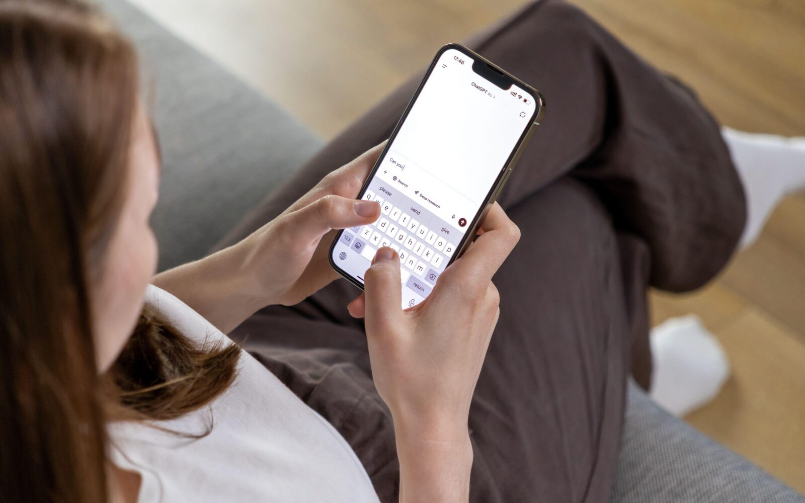 Mlada ženska sedi na kavču in v rokah drži telefon, na katerem se pogovarja s ChatGPT pomočnikom z umetno inteligenco