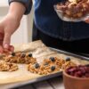 Ženska na pladnju dela domače granola ploščice z oreščki, kosmiči, borovnicami in rozinami - hiter in uravnotežen obrok