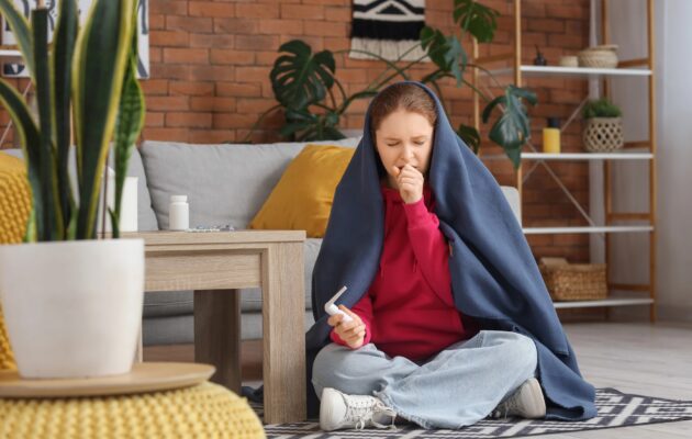 Bolna ženska sedi na tleh, zavita v odejo in kašlja
