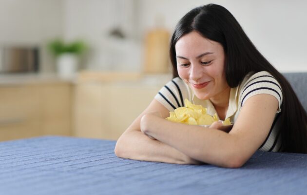 Mlada ženska sedi za mizo in objema skledo slanega čipsa - želja po slanem je lahko simptom različnih zdravstvenih stanj