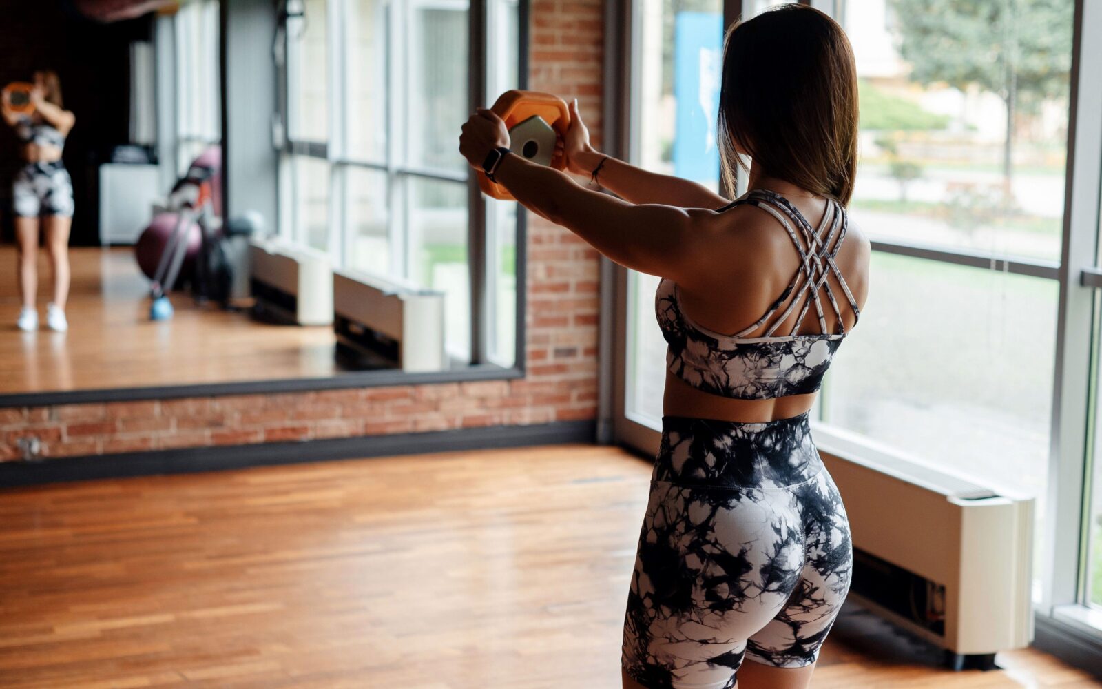 Ženska v fitnesu izvaja vajo za moč z utežjo v rokah, v ozadju je ogledalo