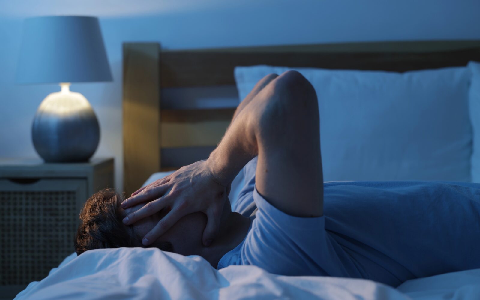 Utrujen moški, ki trpi za nespečnostjo, leži v postelji