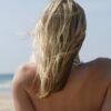 Svetlolasa ženska na plaži, kjer sonce poškoduje lase in pospešuje izsuševanje.