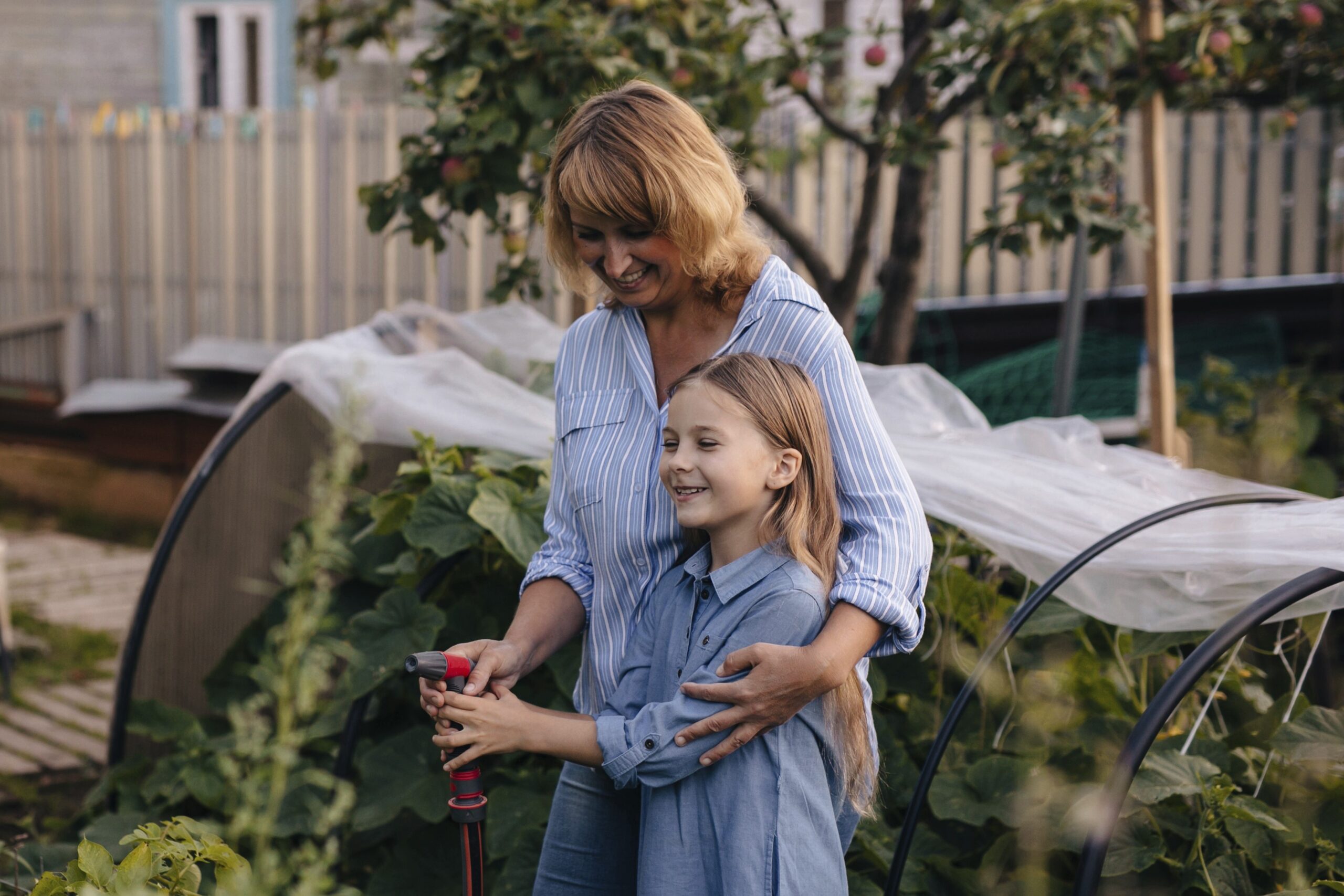 Mama in hči stojita na vrtu in ga zalivata - vrtnarjenje kot koristna aktivnost za povezovanje z drugimi