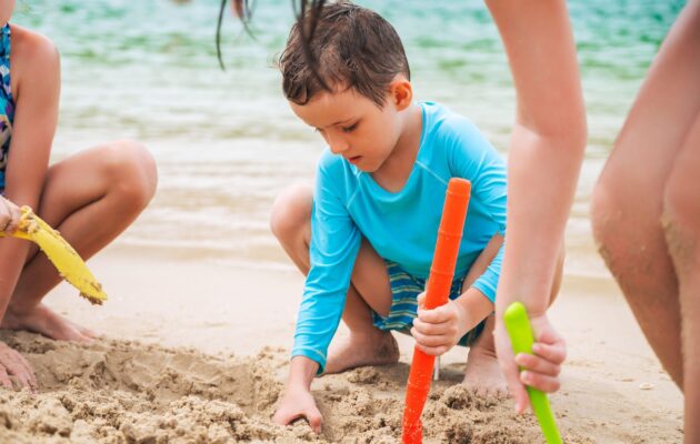 Otrok se igra na plaži in je zaščiten pred UV sevanjem z majico