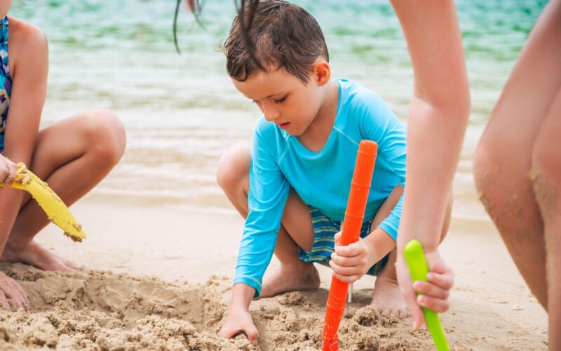 Otrok se igra na plaži in je zaščiten pred UV sevanjem z majico