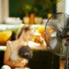 Mlada ženska se hladi z ventilatorjem v pregretem stanovanju med vročinskim valom.