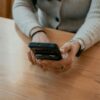 Ženska sedi za mizo in v rokah drži pametni telefon