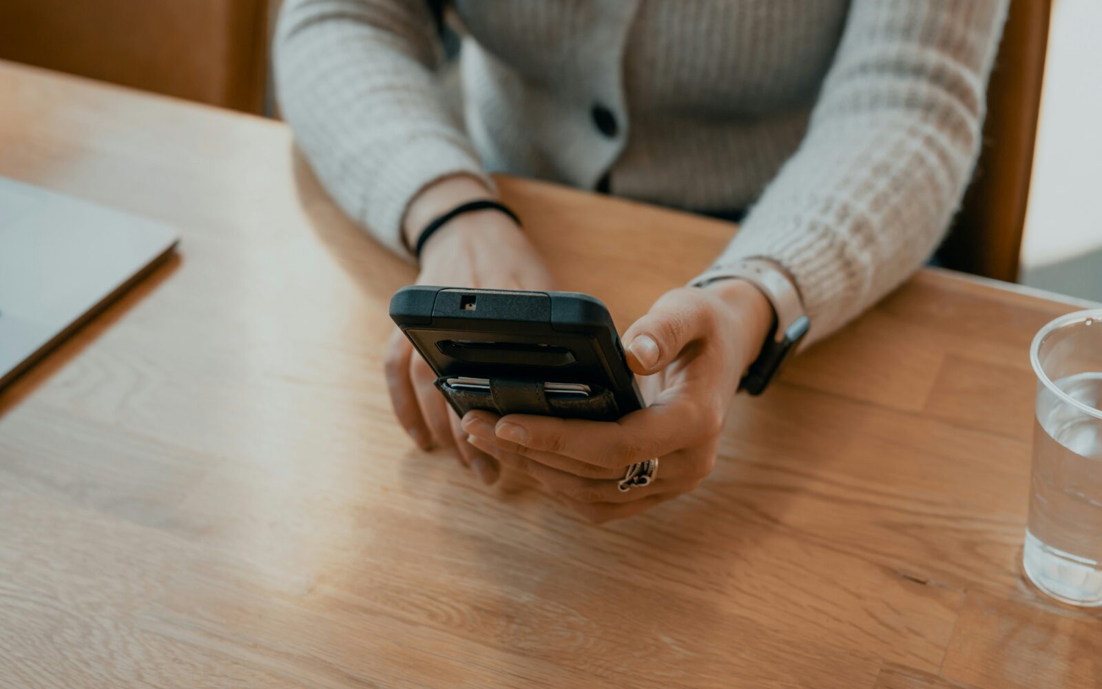 Ženska sedi za mizo in v rokah drži pametni telefon