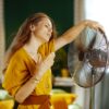 Ženska stoji pred ventilatorjem; trpi zaradi vročinskega vala ali vročinskih oblivov