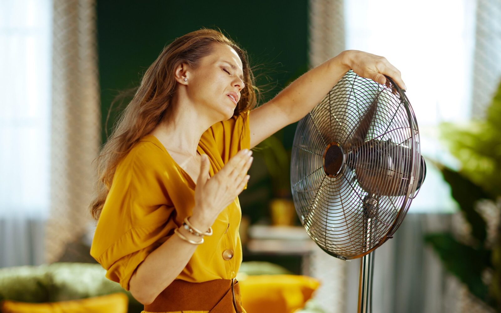 Ženska stoji pred ventilatorjem; trpi zaradi vročinskega vala ali vročinskih oblivov