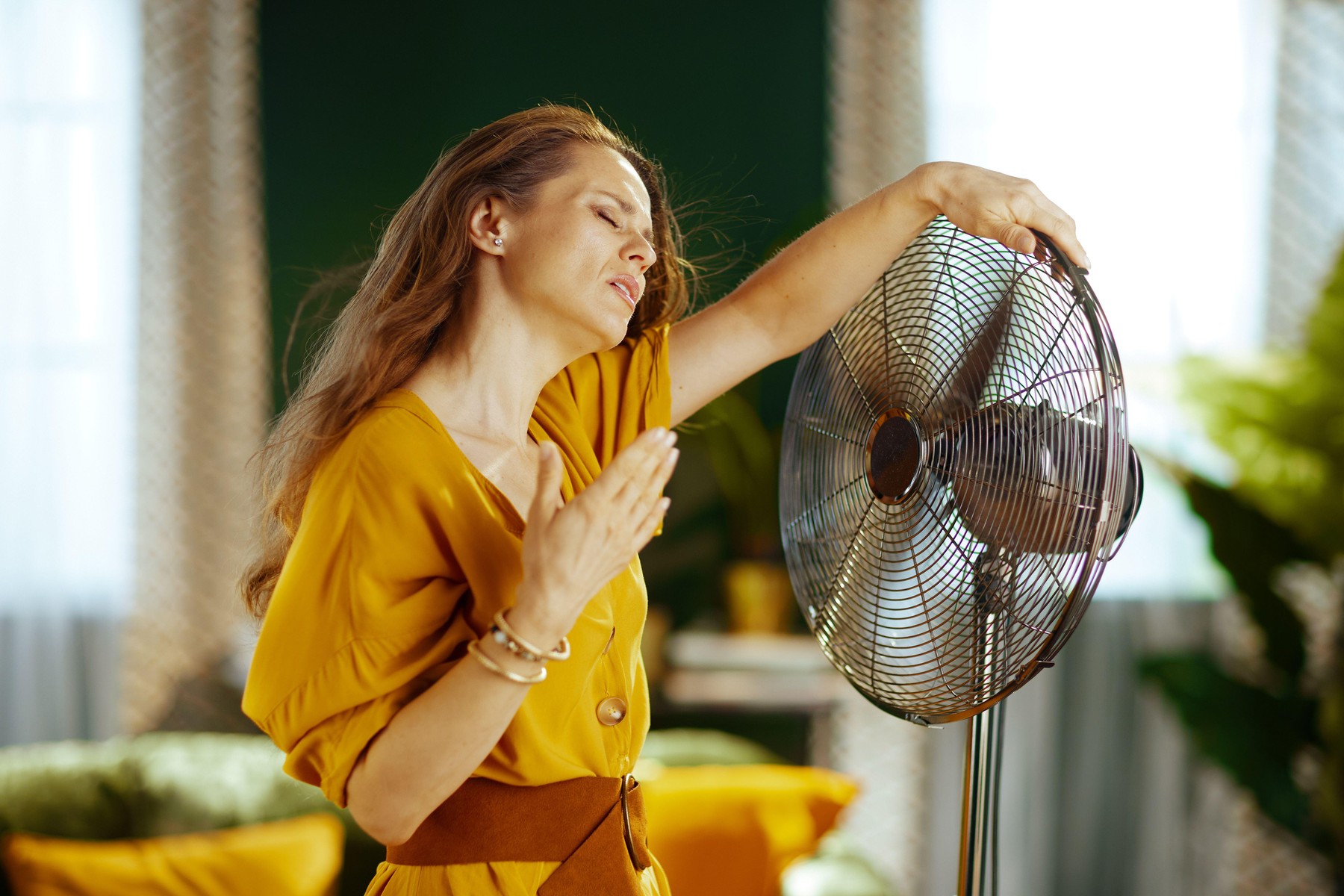 Ženska stoji pred ventilatorjem; trpi zaradi vročinskega vala ali vročinskih oblivov