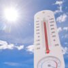 Zunanji termometer prikazuje ekstremno visoke temperature, v ozadju žgoče sonce in modro nebo, ki simbolizirata poletne vročinske valove