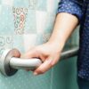 Starejša oseba se z roko oprijema oprijemala na kopalniški steni za večjo varnost in preprečevanje padcev
