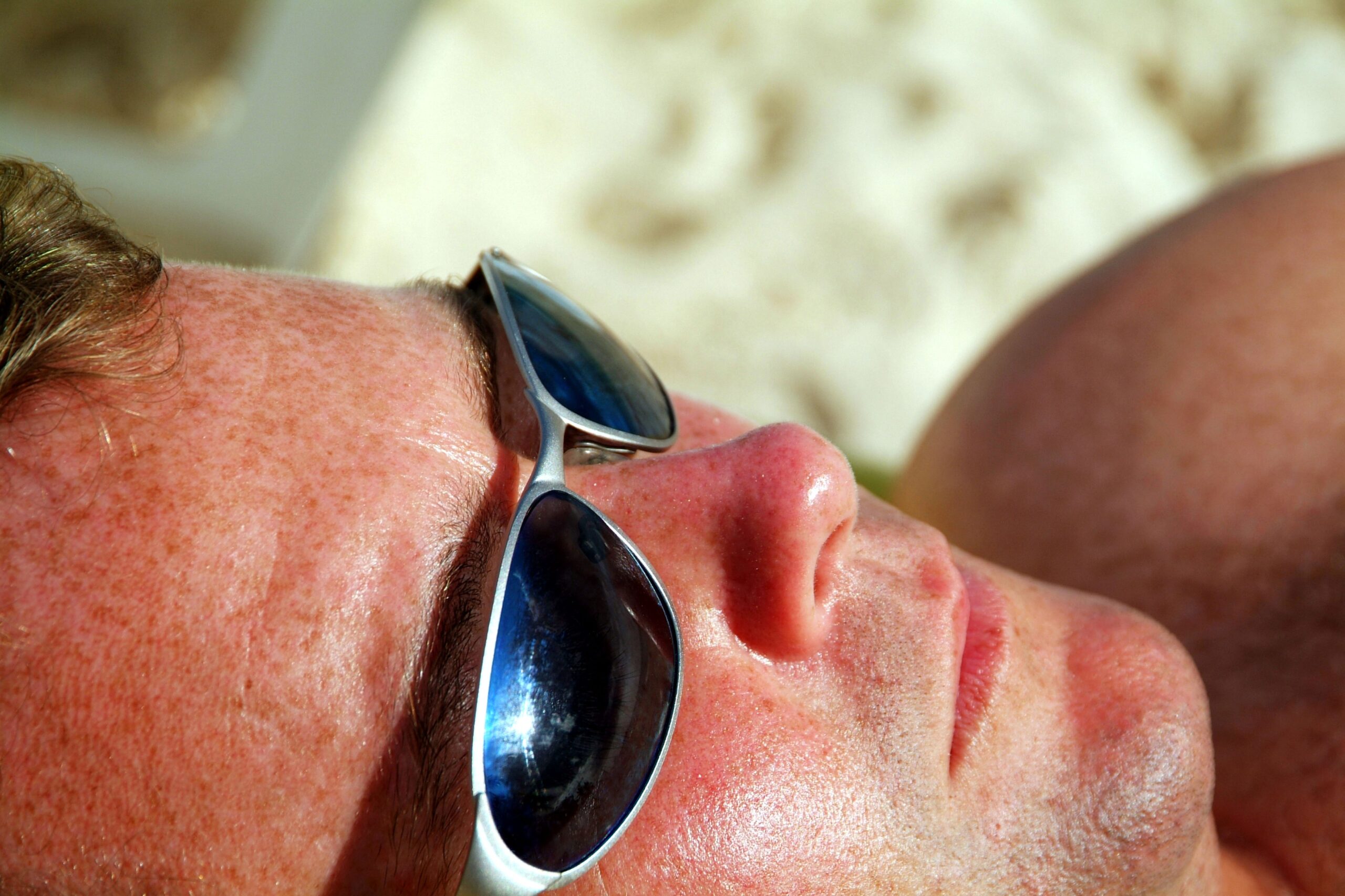 Bližnji posnetek moškega obraza s sončnimi očali - verjetno leži na plaži in je izpostavljen soncu in UV sevanju