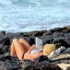 Ženska leži na plaži in polni svoje baterije tako, da bere knjigo.