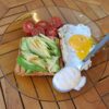 Na mizici je krožnik z zajtrkom - popečen toast kruh, jajca, avokado, češnjev paradižnik in žlica majoneze