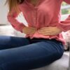 Ženska med menstruacijo drži roke na spodnjem delu trebuha zaradi prebavnih težav in menstrualnih krčev.