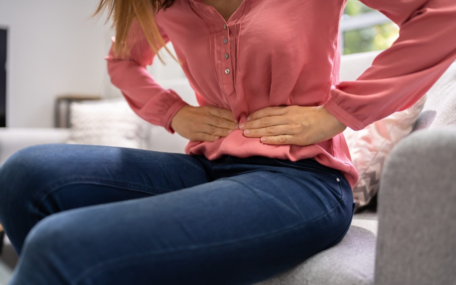 Ženska med menstruacijo drži roke na spodnjem delu trebuha zaradi prebavnih težav in menstrualnih krčev.