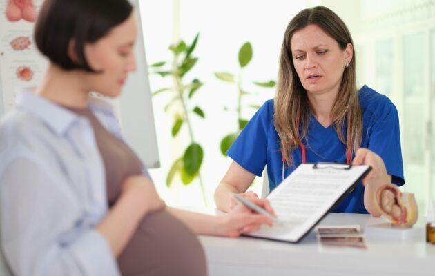 Pregled pacientke v ambulanti ob vodenju zdravstvene dokumentacije. Fotografija ponazarja varovanje zdravstvenih podatkov in dostop do zdravstvenega kartona.