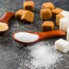 Na mizi so kocke rjavega in kocke belega sladkorja, dve leseni žlici s sladkorjem - kateri sladkor je bolj zdrav?