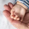 Dojenčkova ročica drži prst odrasle osebe