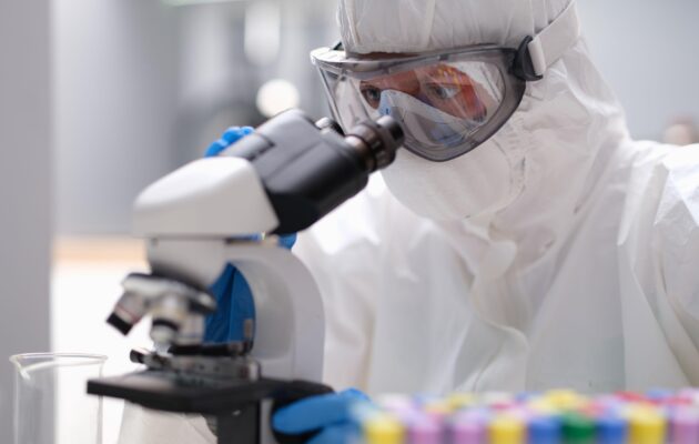 Raziskovalec v zaščitni protikužni obleki med laboratorijskim delom pri preučevanju povzročiteljev kuge